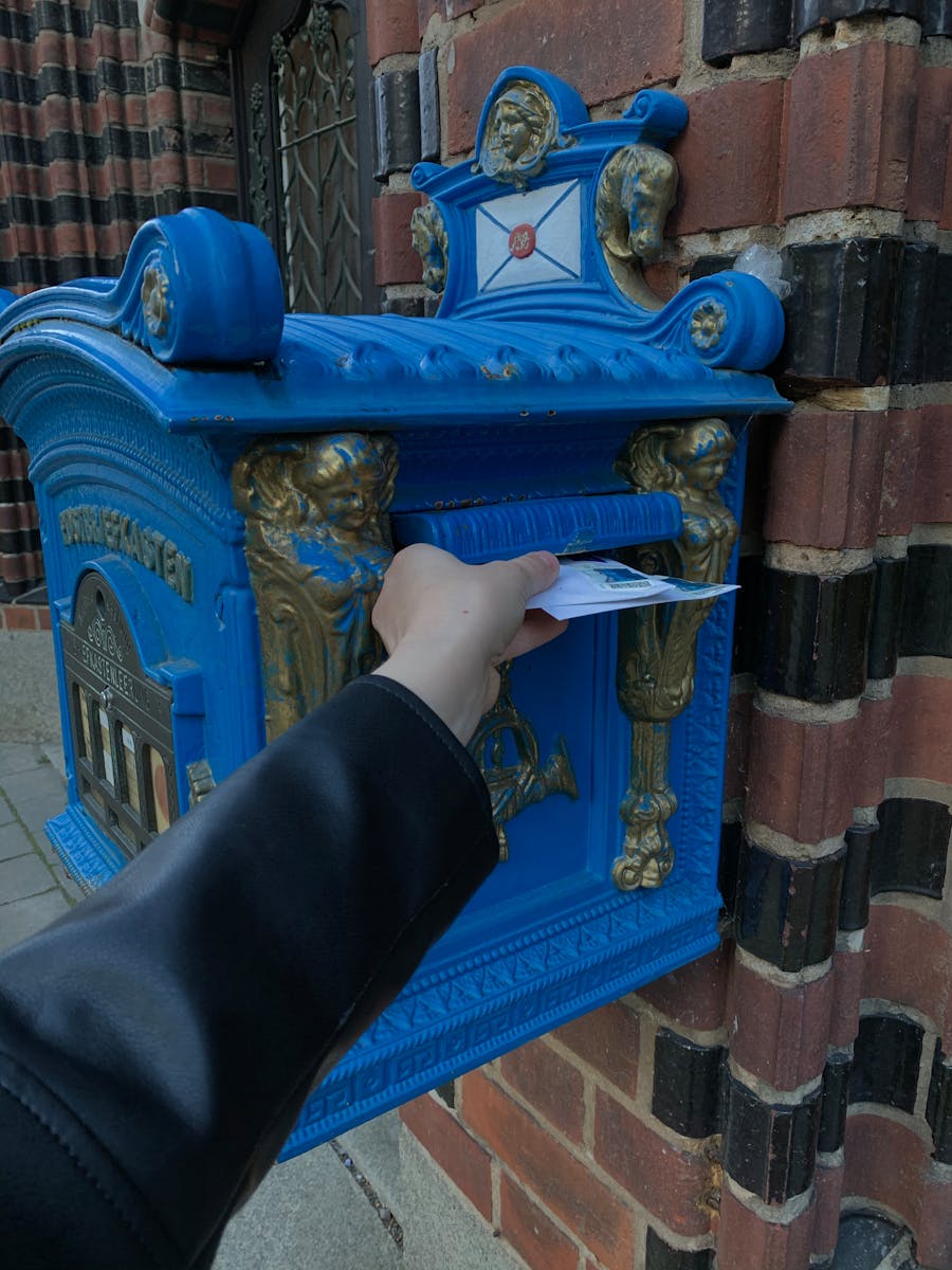 Una mano deposita una carta en un buzón azul